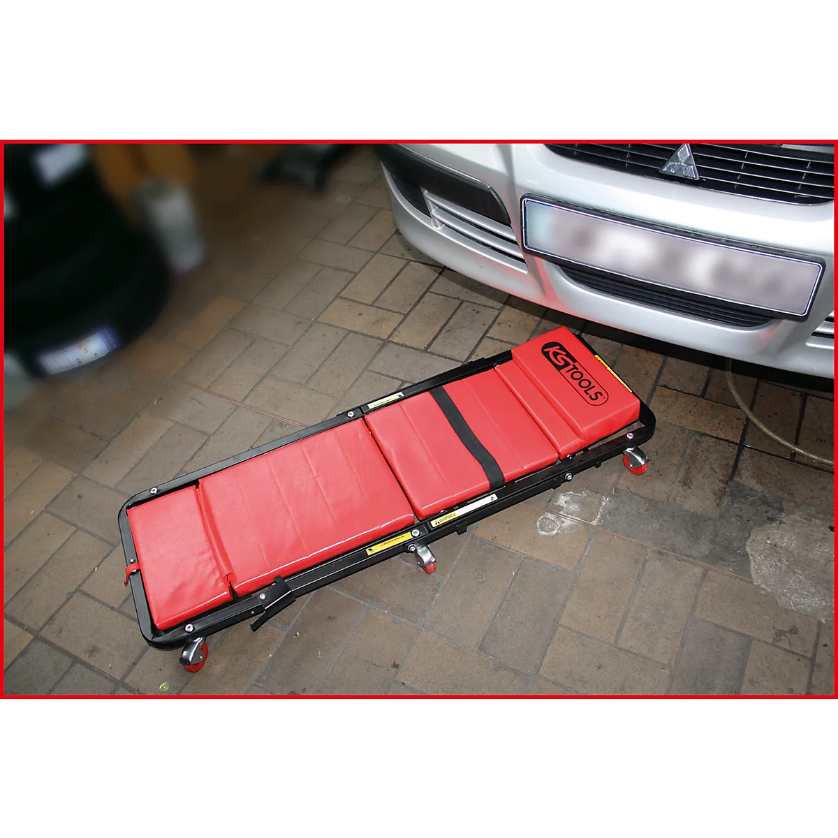 Cric de garage rouge devant une voiture grise.